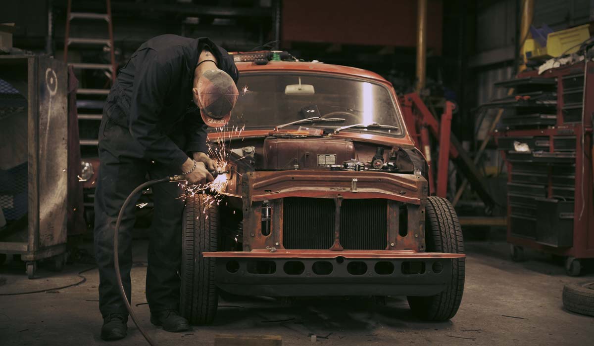 A man welding the front of an old car.